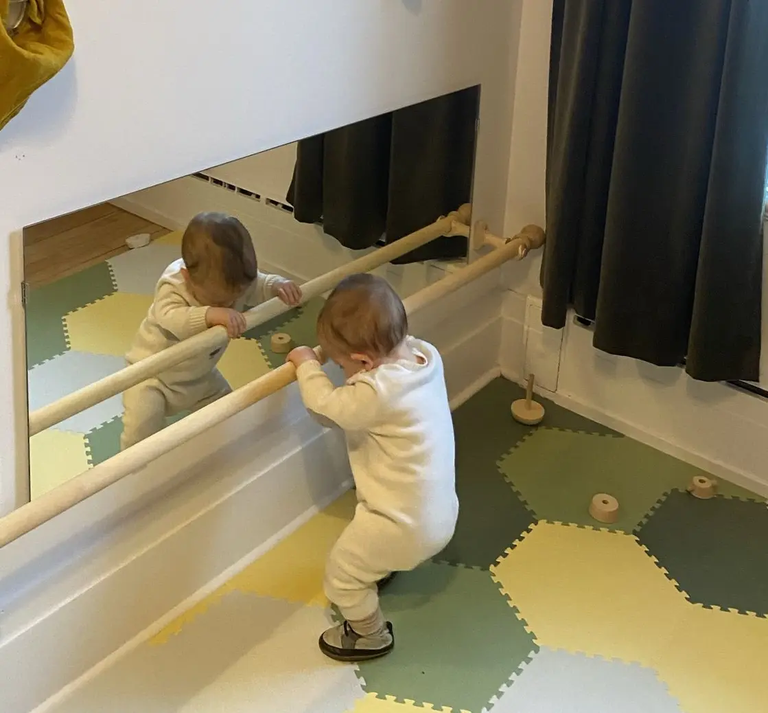 Bébé se hissant à une barre de brachiation Montessori devant un miroir, un aménagement conçu pour soutenir autonomie et motricité